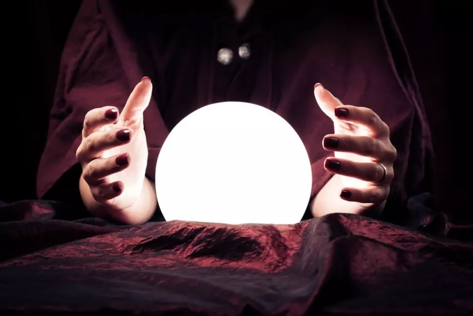 Fortune teller using glowing crystal ball at table indoors, closeup